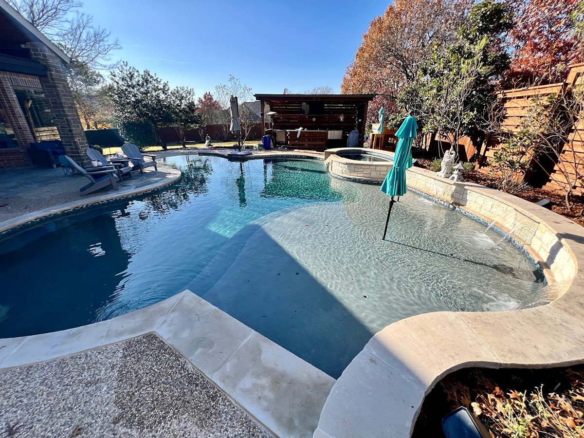 Freeform pool with a tanning ledge, limestone wall with water spouts, spa and covered cabana